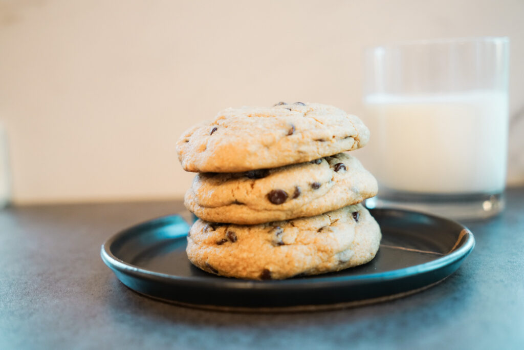 Stack of 3 chocolate chip cookies with milk in the background