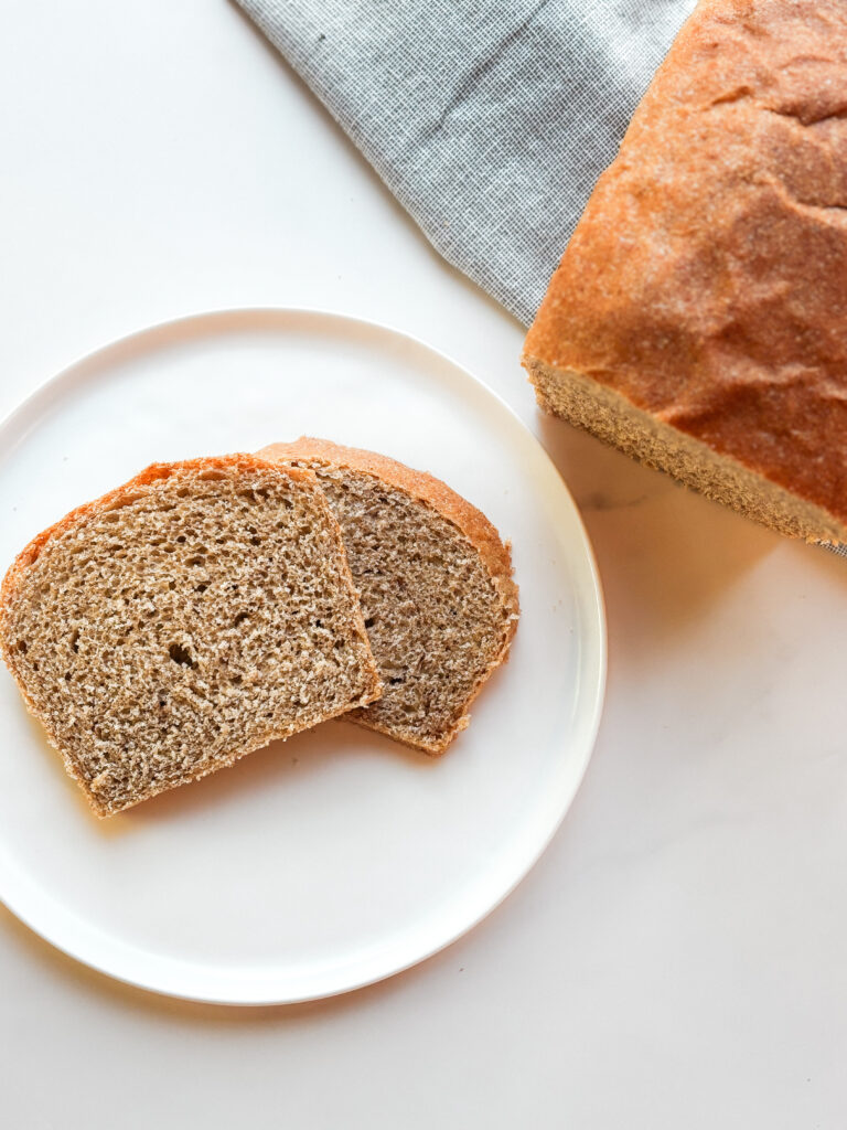Two slices of freshly milled honey wheat bread and a cut loaf of bread on a white table